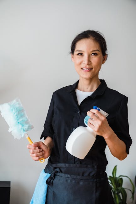 A light blue dustpan with a wooden handle and a natural bristle brush hanging on a hook against a plain, light grey wall. The cleaning tools are clean and well-maintained, arranged neatly to facilitat