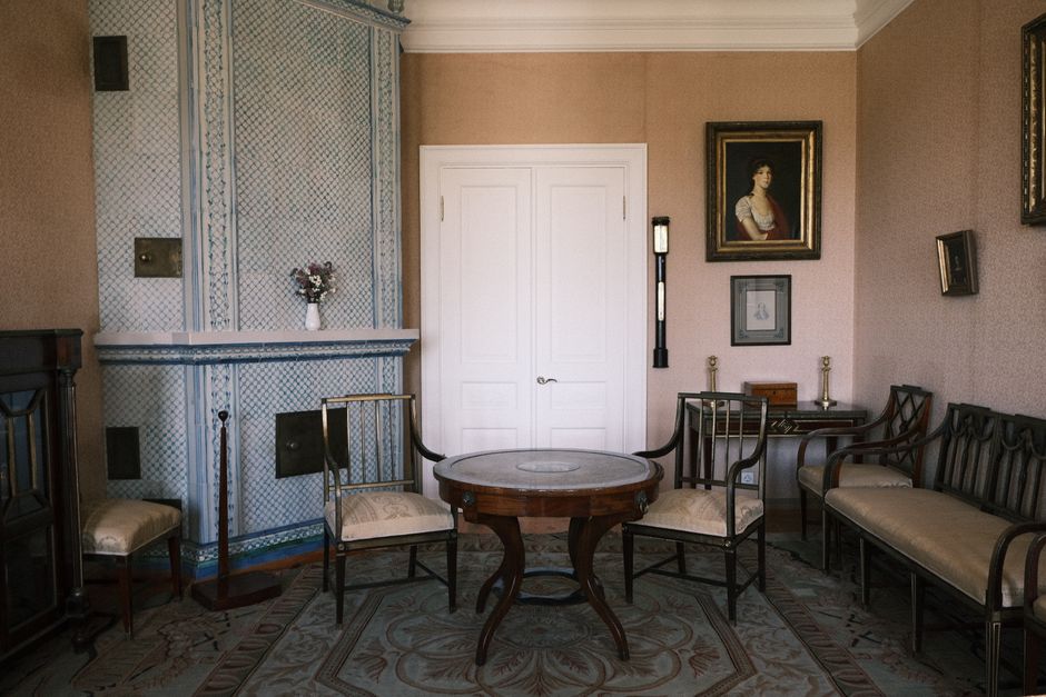 The image depicts a vintage-style living room with classic furnishings and ornate decor. A patterned upholstered sofa with wooden trim is positioned against a wall covered in deep blue wallpaper adorn